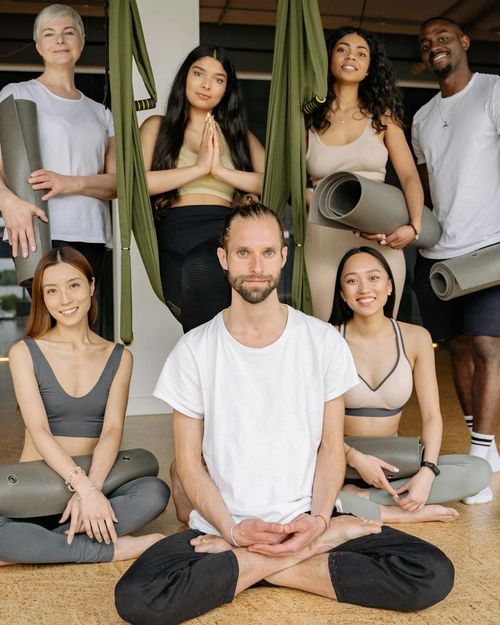 A diverse group of people smiling in a bright yoga studio.